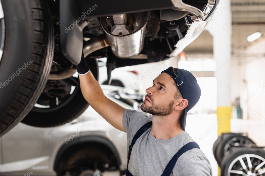 selective focus of handsome mechanic in cap fixing car 