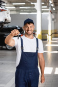 šťastný mechanik v uniformě a čepice drží klíč od auta 