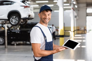 Tulumlu neşeli tamirci ve araba servisinde boş ekranlı dijital tablet tutuyor. 