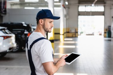 Üniformalı ve başlıklı mekanik atölyede boş ekranlı dijital tablet tutuyor 