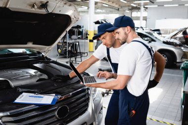 Servis istasyonunda kaputun yanındaki dizüstü bilgisayara bakan oto tamircileri