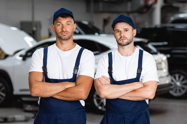 Pohledný Mechanik Uniformě Čepice Stojící Zkříženýma Rukama Autoservisu — Stock fotografie