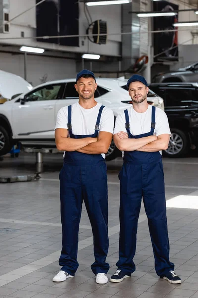 車のサービスで腕を組んで立っているキャップと制服の陽気な力学 — ストック写真