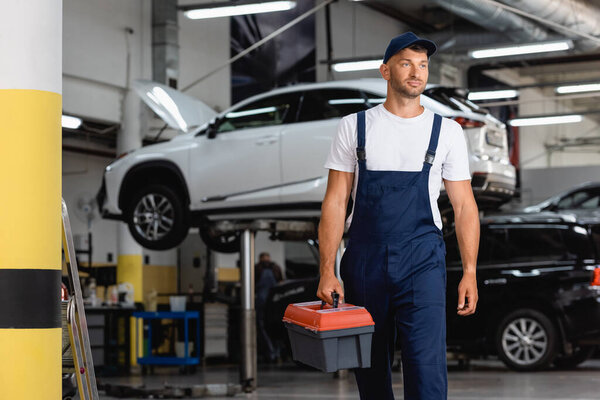 mechanic in uniform and cap holding toolbox in service station