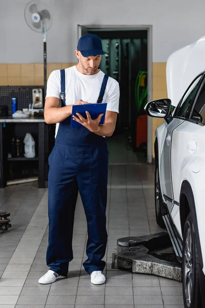 Handsome Mechanic Cap Holding Clipboard Writing Car — Stock Photo, Image