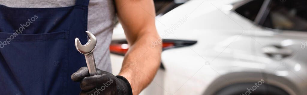 panoramic crop of mechanic in rubber glove holding wrench 