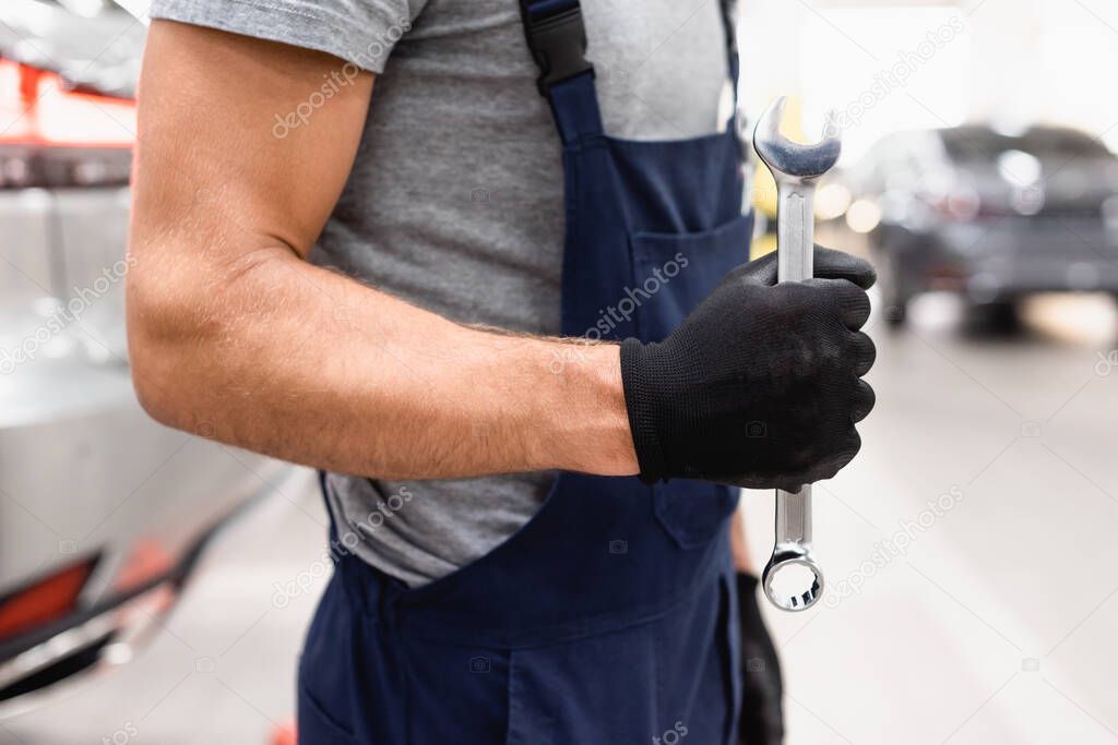 cropped view of mechanic in latex glove and uniform holding wrench 