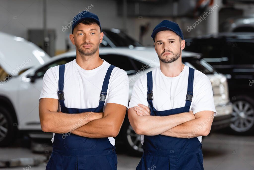 handsome mechanics in uniform and caps standing with crossed arms in car service