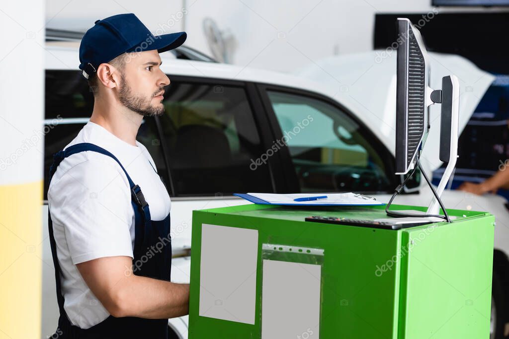 side view of handsome mechanic in cap looking at computer monitor in workshop 