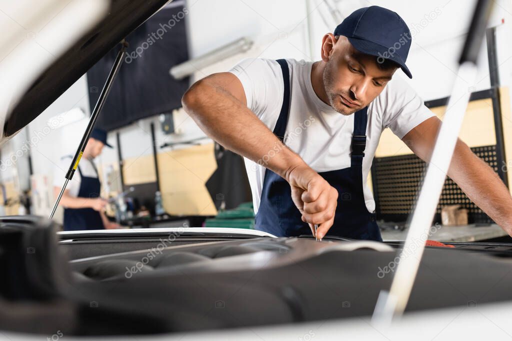 selective focus of mechanic in overalls fixing car near coworker in service station 