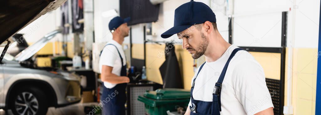 Panoramic shot of auto mechanic in cap and overalls at service station