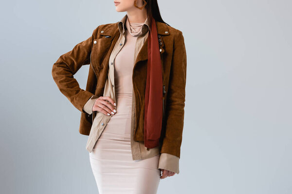 cropped view of fashionable girl in suede jacket posing with hand on hip isolated on grey