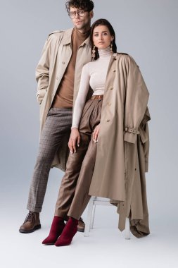 full length view of trendy young couple in autumn clothes looking at camera on grey clipart