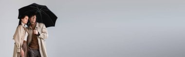 Şemsiye altında dikilip, gri renkten uzaklaşan trend bir çiftin yatay görüntüsü