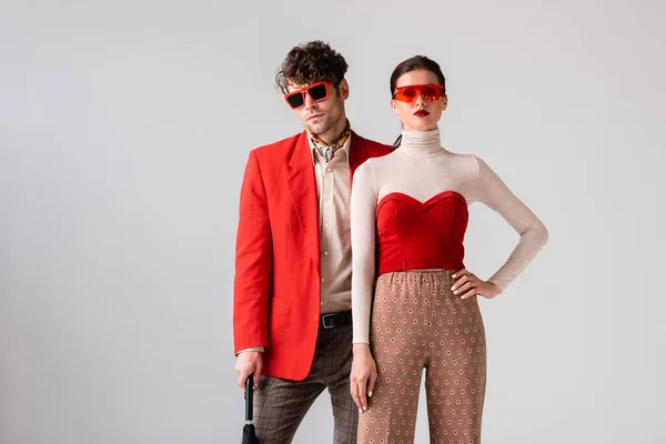 fashionable couple in sunglasses looking at camera isolated on grey