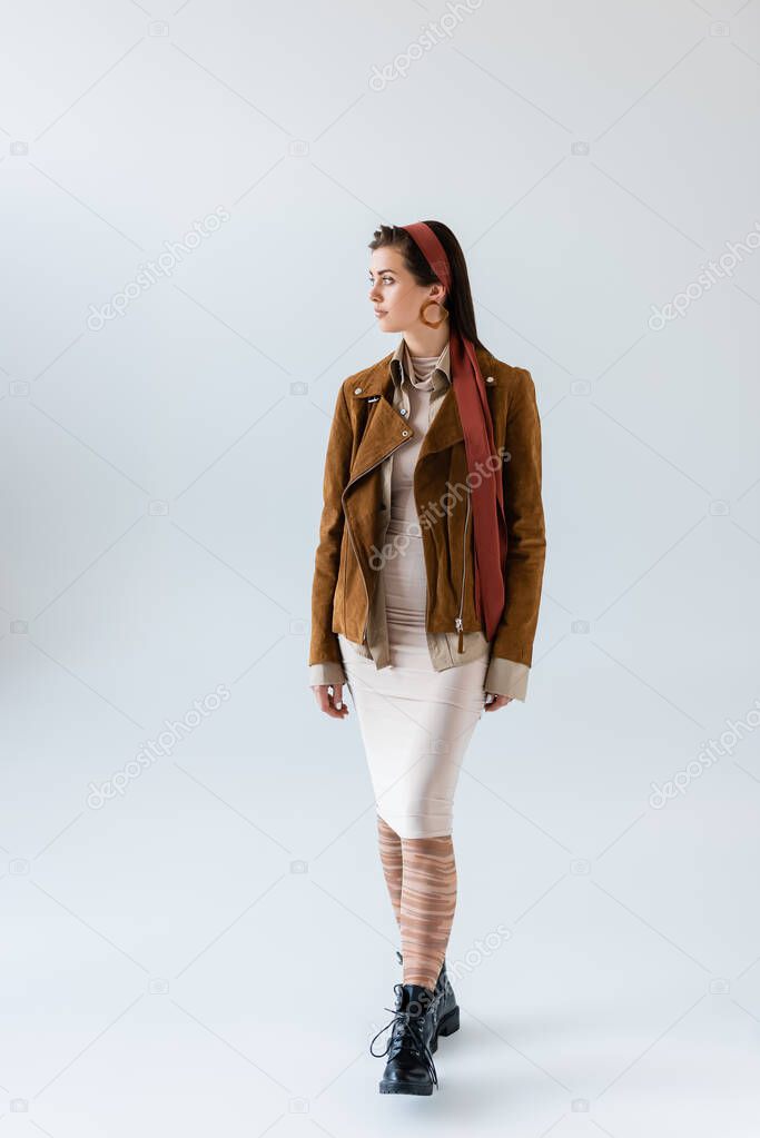 Full length view of attractive, stylish woman in autumn outfit looking away on grey