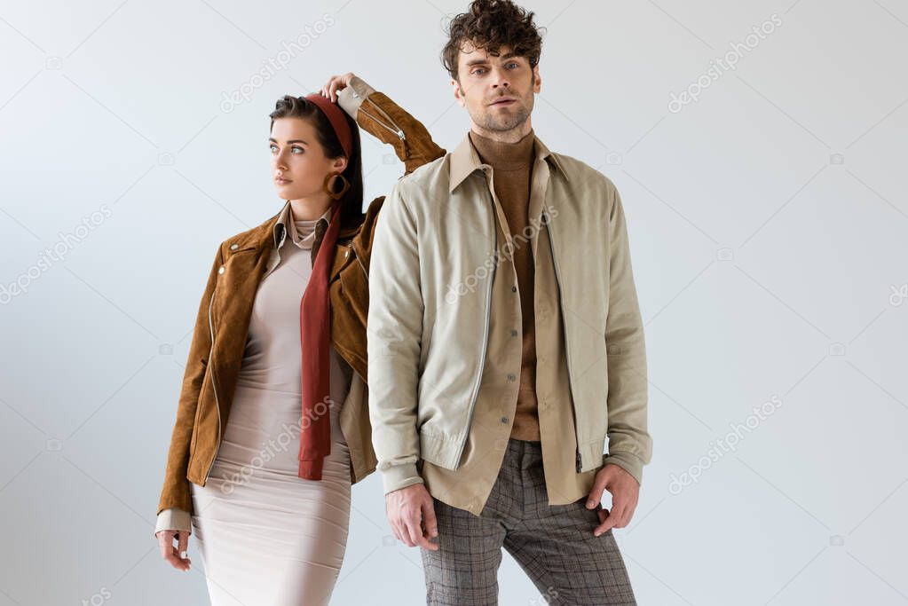 Attractive woman looking away and leaning on handsome man in autumn outfit on grey 