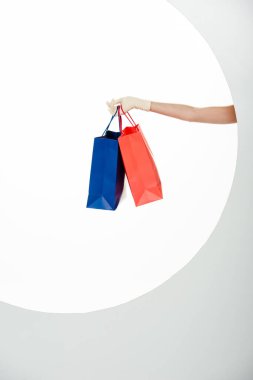 Beyaz arka planda mavi ve kırmızı alışveriş torbaları tutan eldivenli kadın görüntüsü. 