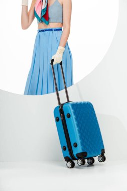 Beyaz arka plandaki yuvarlak deliğin arkasında mavi bavul tutan şık bir kız görüntüsü. 