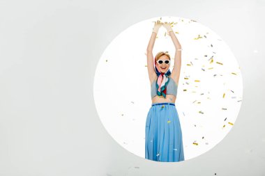 Positive girl in sunglasses standing near circle under falling confetti on white background clipart