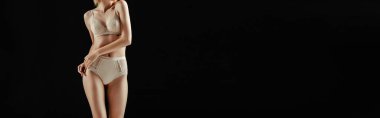 İç çamaşırlı, elleri kalçasına yakın, siyah giyinmiş genç bir kadının panoramik ürünleri. 