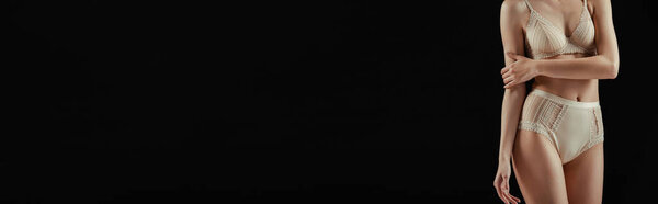 Горизонтальное изображение женщины в нижнем белье, касающейся руки, изолированной на черном 