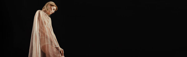 Panoramic shot of blonde woman in underwear and beige chiffon fabric isolated on black 