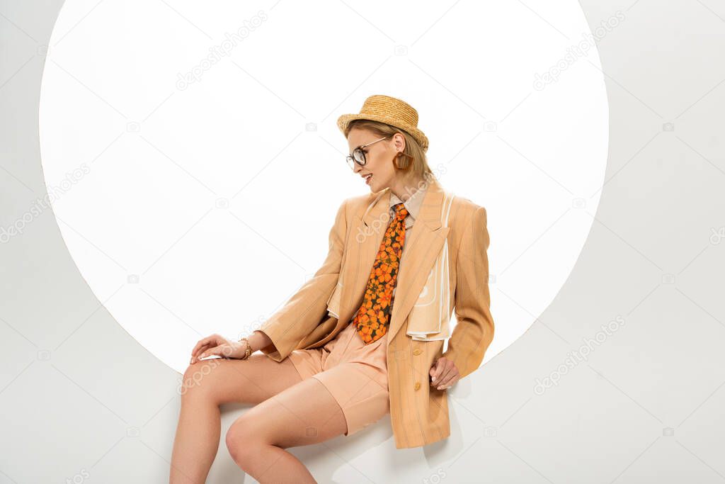 Beautiful smiling woman in eyeglasses and straw hat smiling while sitting in circle on white background 