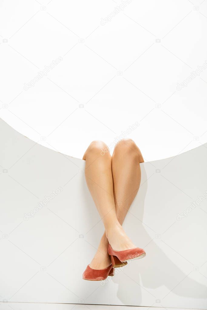 Cropped view of female legs in coral shoes near round hole on white background 