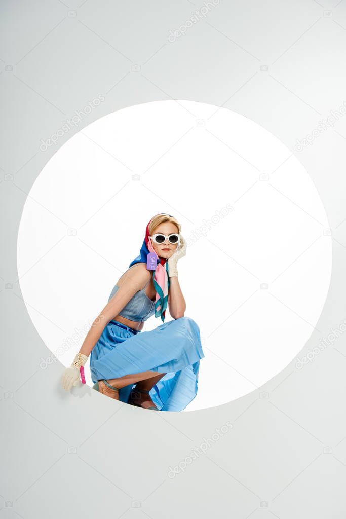 Side view of trendy woman with price tags on clothes posing near circle on white background 