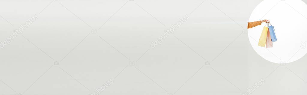 Panoramic shot of woman holding colorful shopping bags behind circle on white background 