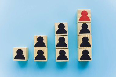Mavi arka planda siyah ve kırmızı insan simgeleri, liderlik ve kariyer merdiveni kavramına sahip ahşap blokların üst görünümü