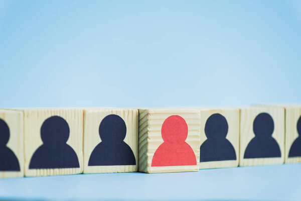row of wooden blocks with black and red human icons on blue background, leadership concept 