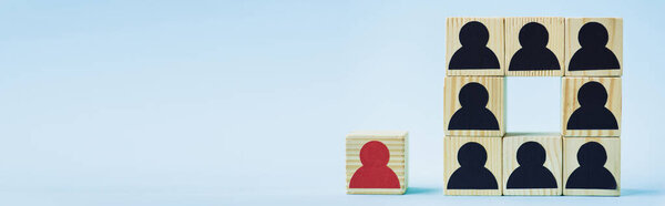 square of wooden blocks with black human icons and red piece on blue background, leadership concept, panoramic shot