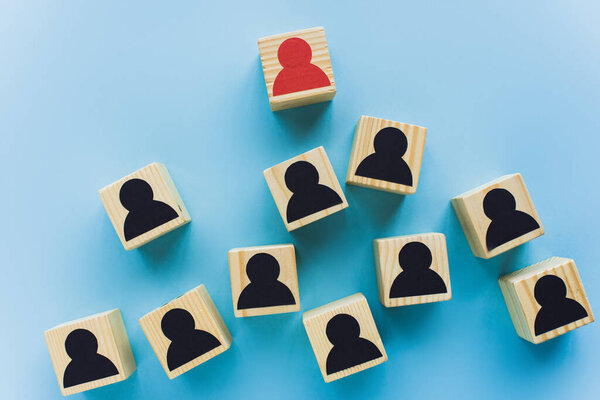 top view of wooden blocks with black and red human icons scattered on blue background, leadership concept