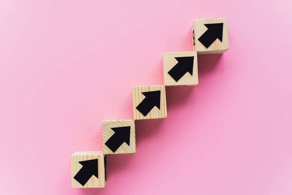 top view of wooden blocks with black arrows on pink background, business concept 