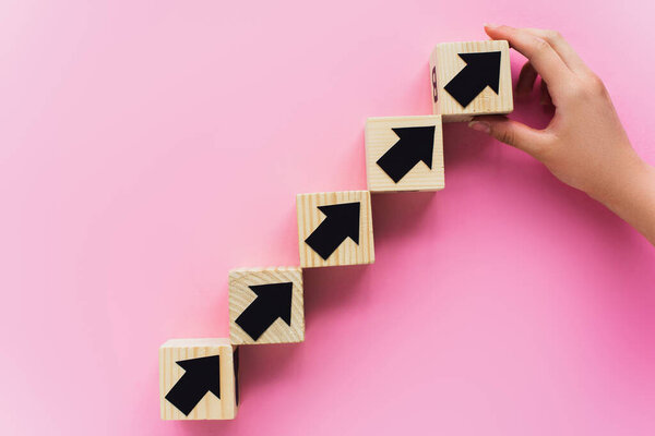 partial view of hand near wooden blocks with black arrows on pink background, business concept 