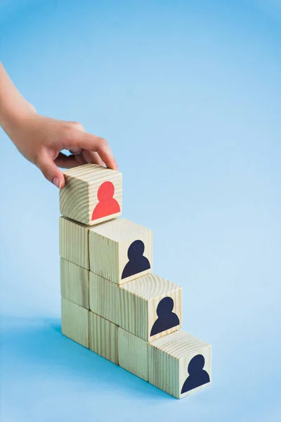 Cropped view of hand touching pyramid of wooden blocks with black and red human icons on blue background, leadership concept — Stock Image Cropped View Hand Touching Pyramid Wooden Blocks Black Red Human Stock Photo