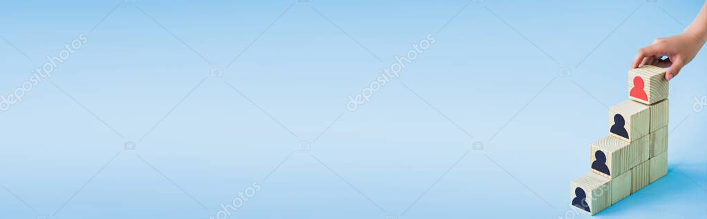 Cropped view of hand touching pyramid of wooden blocks with black and red human icons on blue background, leadership concept — Stock Image Cropped View Hand Touching Pyramid Wooden Blocks Black Red Human Stock Photo