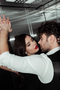 Yakışıklı adam asansörde güzel bir kadını öpüyor.
