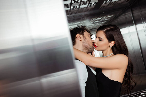 Selective focus of beautiful woman with red lips kissing boyfriend in elevator