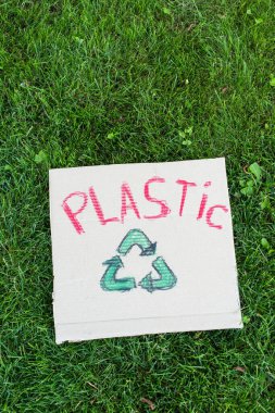 Çimlerin üzerinde plastik harf ve geri dönüşüm işareti olan afişin üst görünümü, ekoloji kavramı