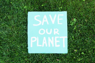 Top view of save our planet lettering on placard on green grass, ecology concept clipart