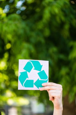 Cropped view of man holding card with recycle sign outdoors, ecology concept clipart