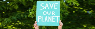 Panoramic shot of man holding placard with save our planet lettering with trees at background, ecology concept clipart