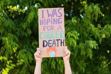 Cropped view of man holding placard with i was hoping for a cooler death lettering with trees at background, ecology concept clipart
