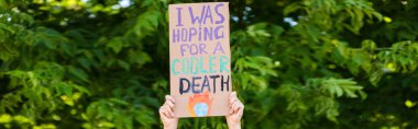 Panoramic orientation of man holding placard with i was hoping for a cooler death lettering with trees at background, ecology concept  clipart
