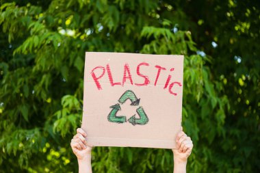 Plastik geri dönüşüm tabelalı, arka planda ağaçlı, ekoloji konsepti olan bir adamın kısmi görünümü
