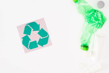 Kartın yanındaki plastik şişelerin ve kozmetik paketlerin beyaz zemin üzerinde geri dönüşüm işareti olan üst görünümü, ekoloji kavramı