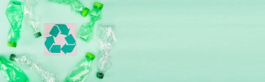 Panoramic concept of crumpled plastic bottles near card with recycle symbol on green background, ecology concept clipart